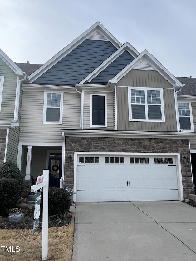 townhome / multi-family property with a garage, stone siding, driveway, and board and batten siding