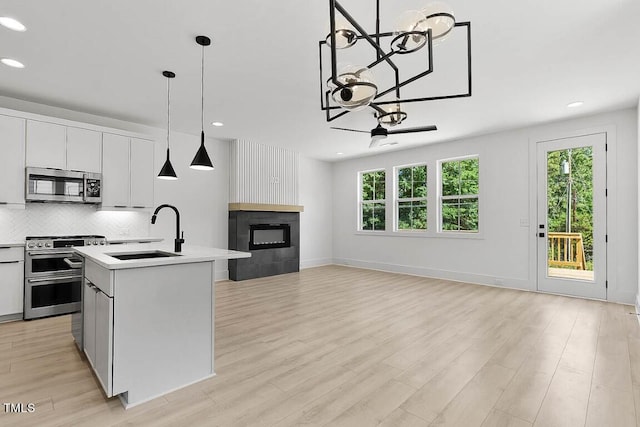 kitchen with stainless steel appliances, a kitchen island with sink, sink, and white cabinets