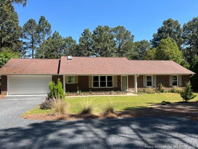 ranch-style home featuring an attached garage, brick siding, a front yard, and gravel driveway