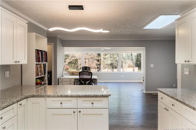 kitchen with crown molding, dark wood-style flooring, a peninsula, baseboards, and a skylight