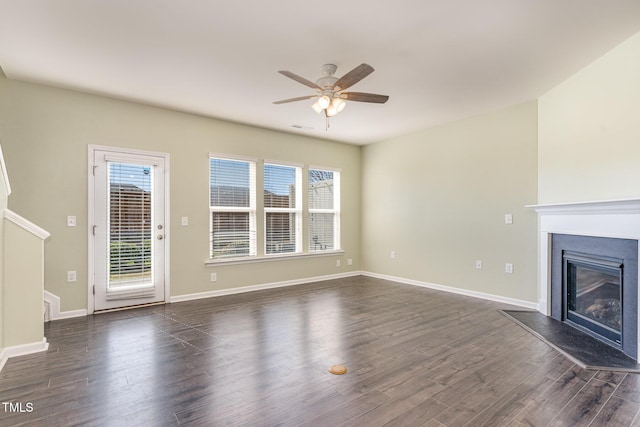 unfurnished living room featuring a ceiling fan, a glass covered fireplace, dark wood finished floors, and baseboards