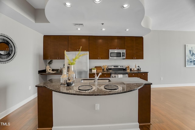 kitchen featuring stainless steel appliances, visible vents, a sink, an island with sink, and wood finished floors