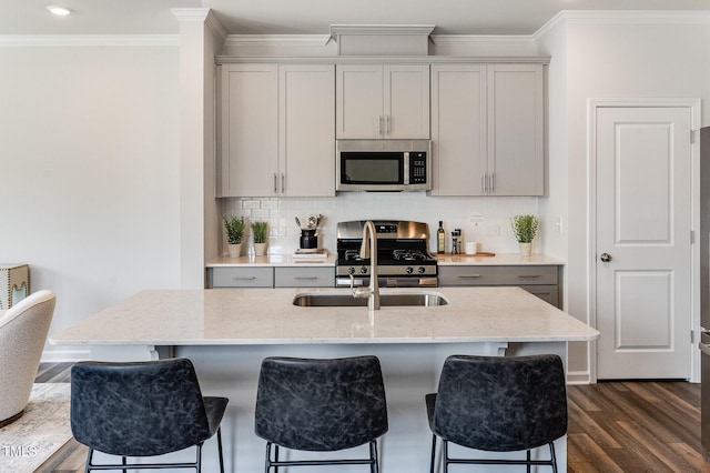 kitchen featuring stainless steel appliances, gray cabinets, a kitchen island with sink, and light stone counters