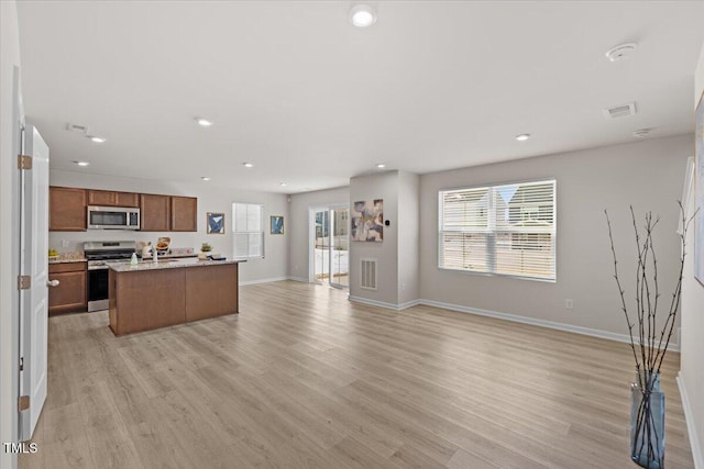 kitchen with stainless steel appliances, light wood-style floors, open floor plan, brown cabinets, and a center island with sink