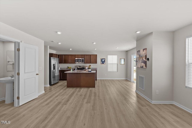 kitchen with appliances with stainless steel finishes, open floor plan, a center island, light countertops, and light wood-style floors