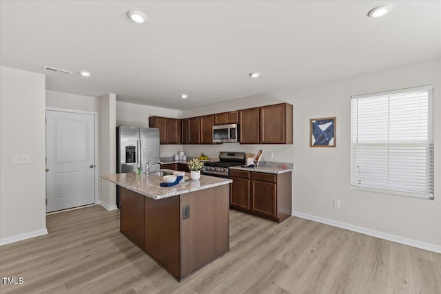 kitchen with appliances with stainless steel finishes, baseboards, a kitchen island with sink, and light wood finished floors