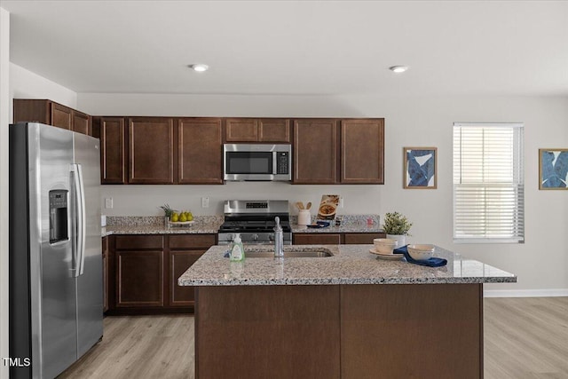 kitchen featuring stainless steel appliances, light stone counters, a center island with sink, and dark brown cabinetry