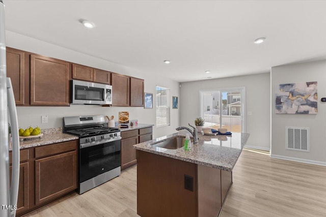 kitchen with a center island with sink, visible vents, appliances with stainless steel finishes, light stone countertops, and a sink