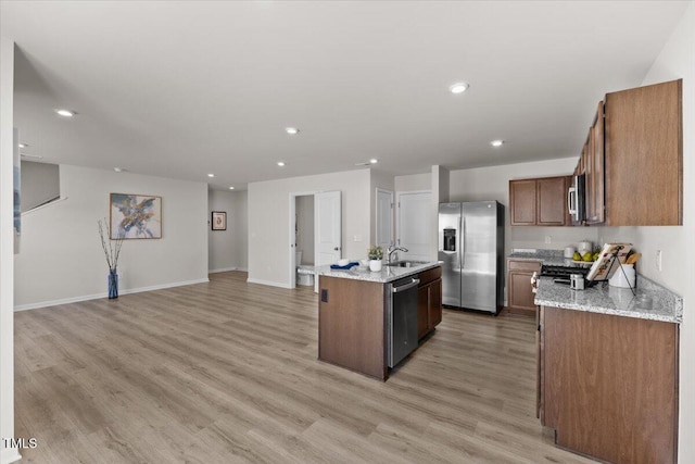 kitchen with stainless steel appliances, a sink, light wood-style floors, open floor plan, and an island with sink