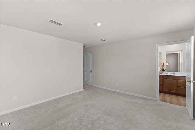 unfurnished bedroom with ensuite bathroom, light carpet, a sink, visible vents, and baseboards