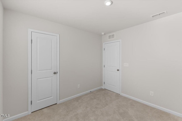 empty room featuring light colored carpet, visible vents, and baseboards