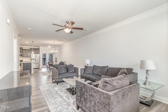 living room with ornamental molding, light wood-style flooring, baseboards, and ceiling fan with notable chandelier