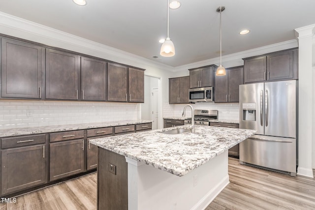 kitchen with dark brown cabinetry, stainless steel appliances, a sink, light stone countertops, and light wood finished floors