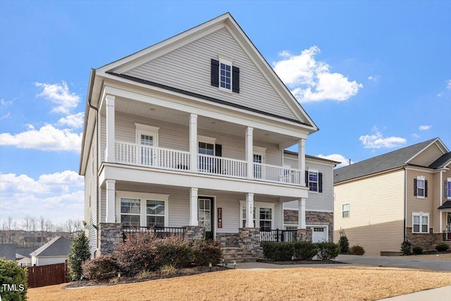 neoclassical / greek revival house with a balcony, covered porch, and stone siding