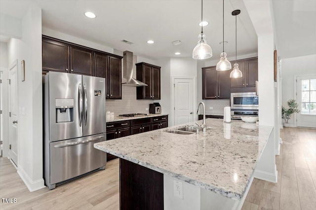 kitchen with stainless steel appliances, a sink, visible vents, wall chimney range hood, and light wood finished floors