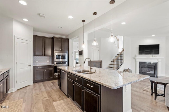 kitchen with stainless steel appliances, a sink, decorative backsplash, light wood finished floors, and a glass covered fireplace