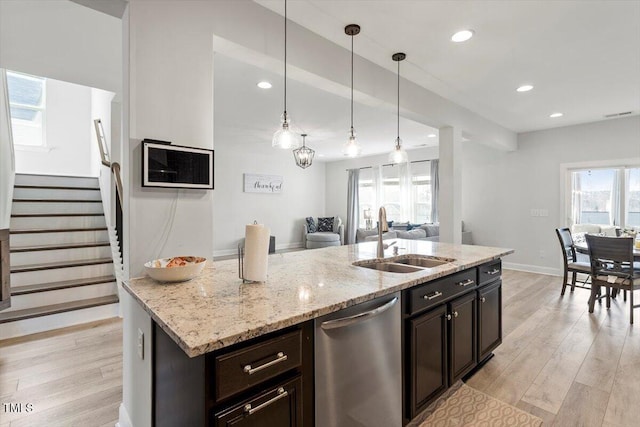 kitchen with light wood finished floors, open floor plan, hanging light fixtures, stainless steel dishwasher, and a sink