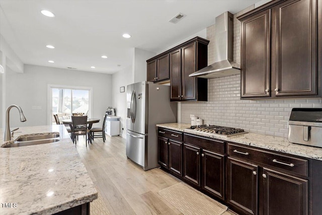 kitchen featuring stainless steel appliances, a sink, visible vents, light wood-style floors, and wall chimney range hood