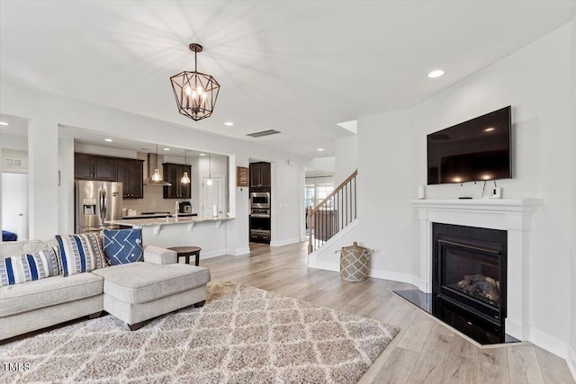 living area with visible vents, a glass covered fireplace, light wood-type flooring, baseboards, and stairs