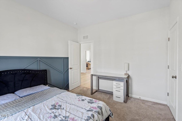 bedroom featuring visible vents, a decorative wall, carpet flooring, and wainscoting