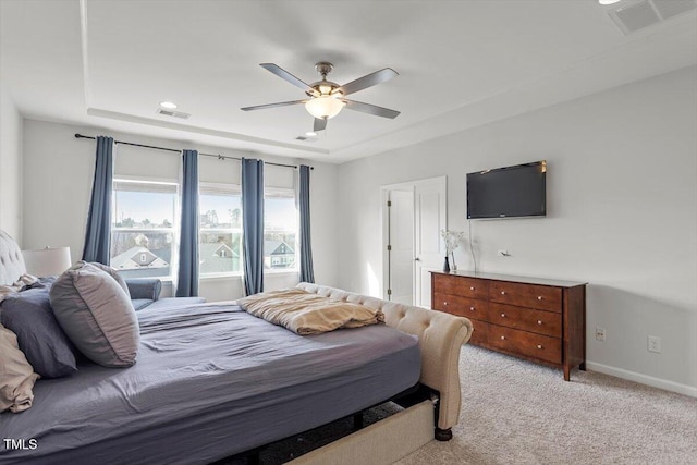 bedroom featuring light colored carpet, baseboards, visible vents, and a tray ceiling