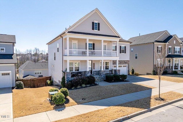 view of front of house with covered porch, concrete driveway, a balcony, a garage, and stone siding