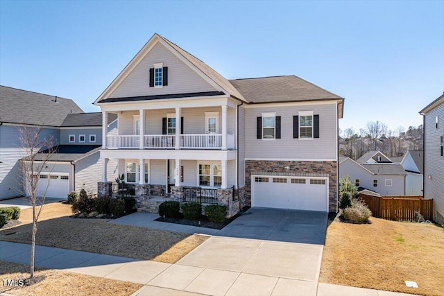 view of front of house with an attached garage, a balcony, covered porch, driveway, and stone siding