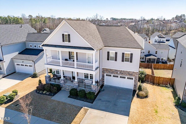 traditional-style home featuring a porch, a balcony, fence, concrete driveway, and stone siding