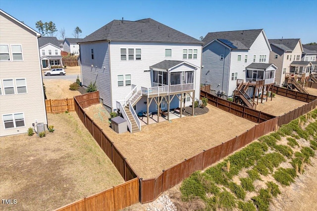 rear view of house featuring a sunroom, a fenced backyard, a residential view, stairs, and a yard