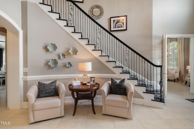 stairs featuring tile patterned floors, baseboards, arched walkways, and a towering ceiling