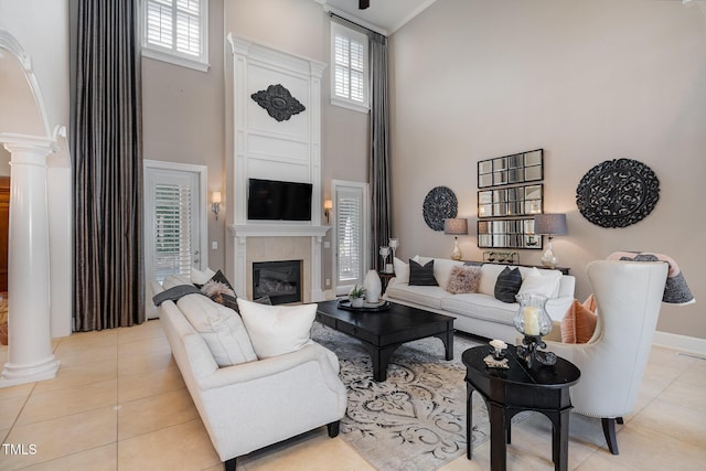 living room featuring a high ceiling, a fireplace, tile patterned flooring, decorative columns, and baseboards