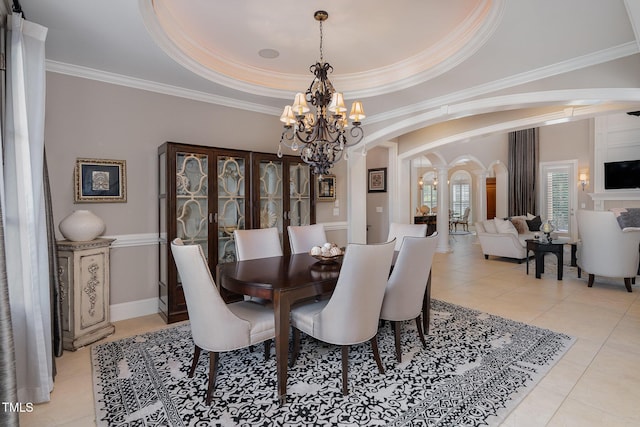 dining area with a tray ceiling, arched walkways, an inviting chandelier, light tile patterned floors, and decorative columns