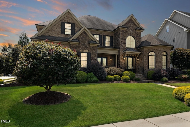 view of front of house with stone siding, brick siding, a lawn, and a shingled roof