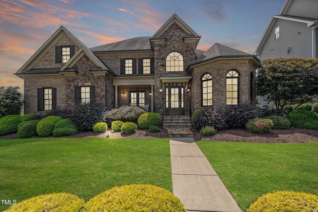 french provincial home with brick siding and a yard