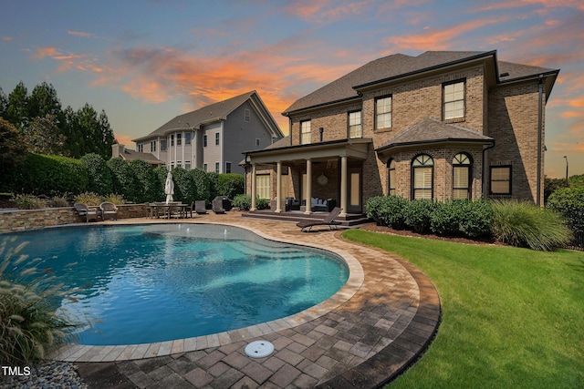 pool at dusk featuring an outdoor pool, a yard, and a patio