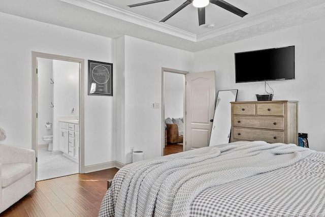 bedroom with connected bathroom, hardwood / wood-style flooring, ceiling fan, a tray ceiling, and crown molding