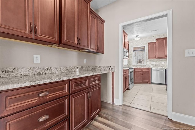 kitchen featuring light stone counters, appliances with stainless steel finishes, light hardwood / wood-style flooring, and backsplash