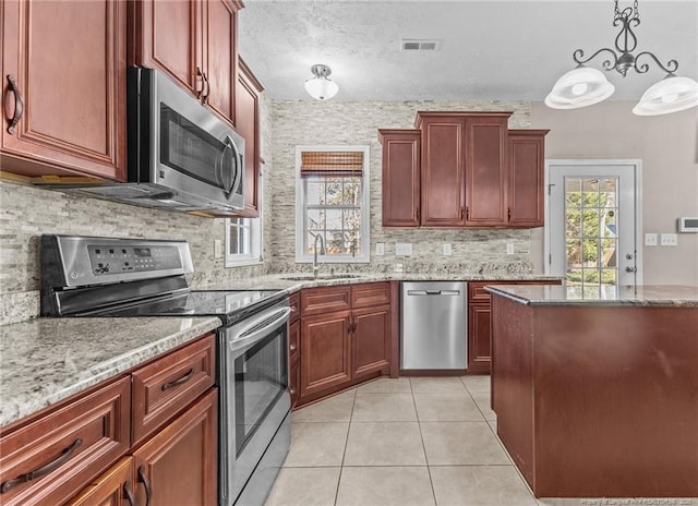 kitchen with pendant lighting, sink, light tile patterned floors, stainless steel appliances, and light stone countertops