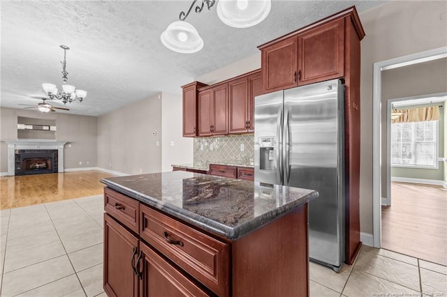 kitchen with tasteful backsplash, stainless steel fridge, dark stone counters, hanging light fixtures, and a center island