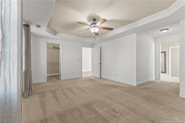 unfurnished bedroom featuring a raised ceiling, crown molding, a spacious closet, and light colored carpet