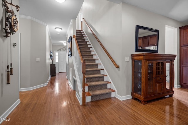 staircase with baseboards, ornamental molding, and wood finished floors