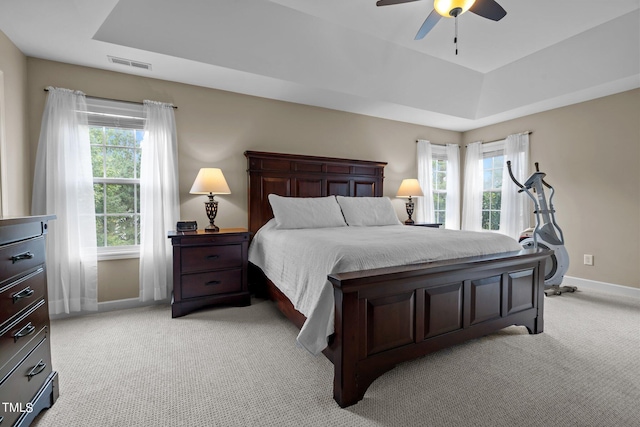 bedroom featuring light colored carpet, a tray ceiling, visible vents, and multiple windows