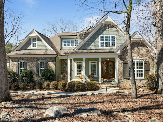 view of front facade featuring stone siding, a shingled roof, and a porch