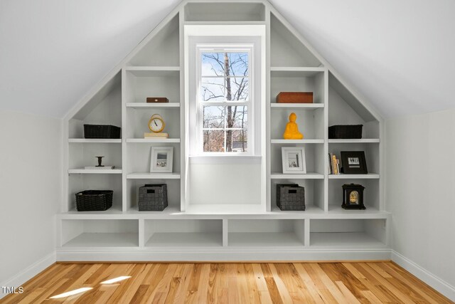 additional living space with lofted ceiling, built in shelves, baseboards, and wood finished floors