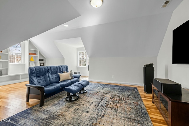 living room with light wood finished floors, built in shelves, visible vents, and vaulted ceiling