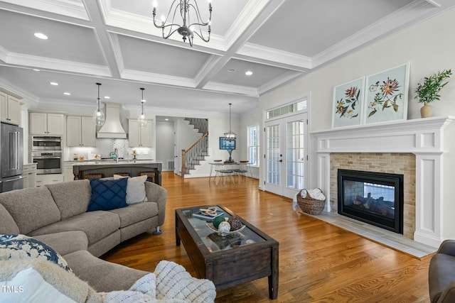 living area featuring french doors, stairway, coffered ceiling, and wood finished floors