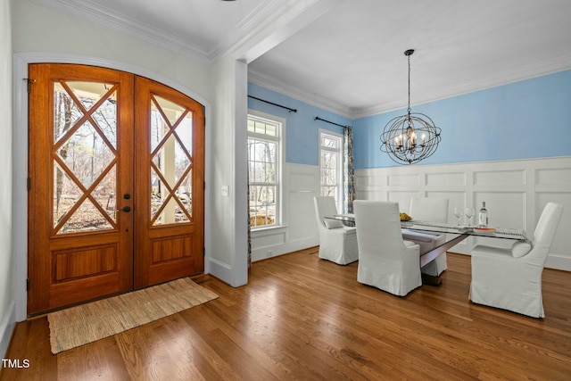 unfurnished dining area with french doors, a notable chandelier, ornamental molding, wainscoting, and wood finished floors