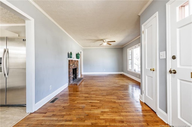 unfurnished living room featuring ornamental molding, ceiling fan, a brick fireplace, a textured ceiling, and light hardwood / wood-style flooring