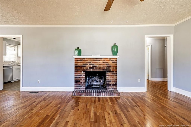 unfurnished living room with crown molding, ceiling fan, hardwood / wood-style floors, a textured ceiling, and a brick fireplace