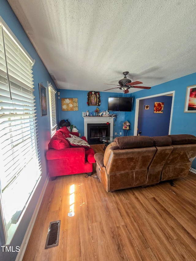 living room with hardwood / wood-style flooring, ceiling fan, and a textured ceiling